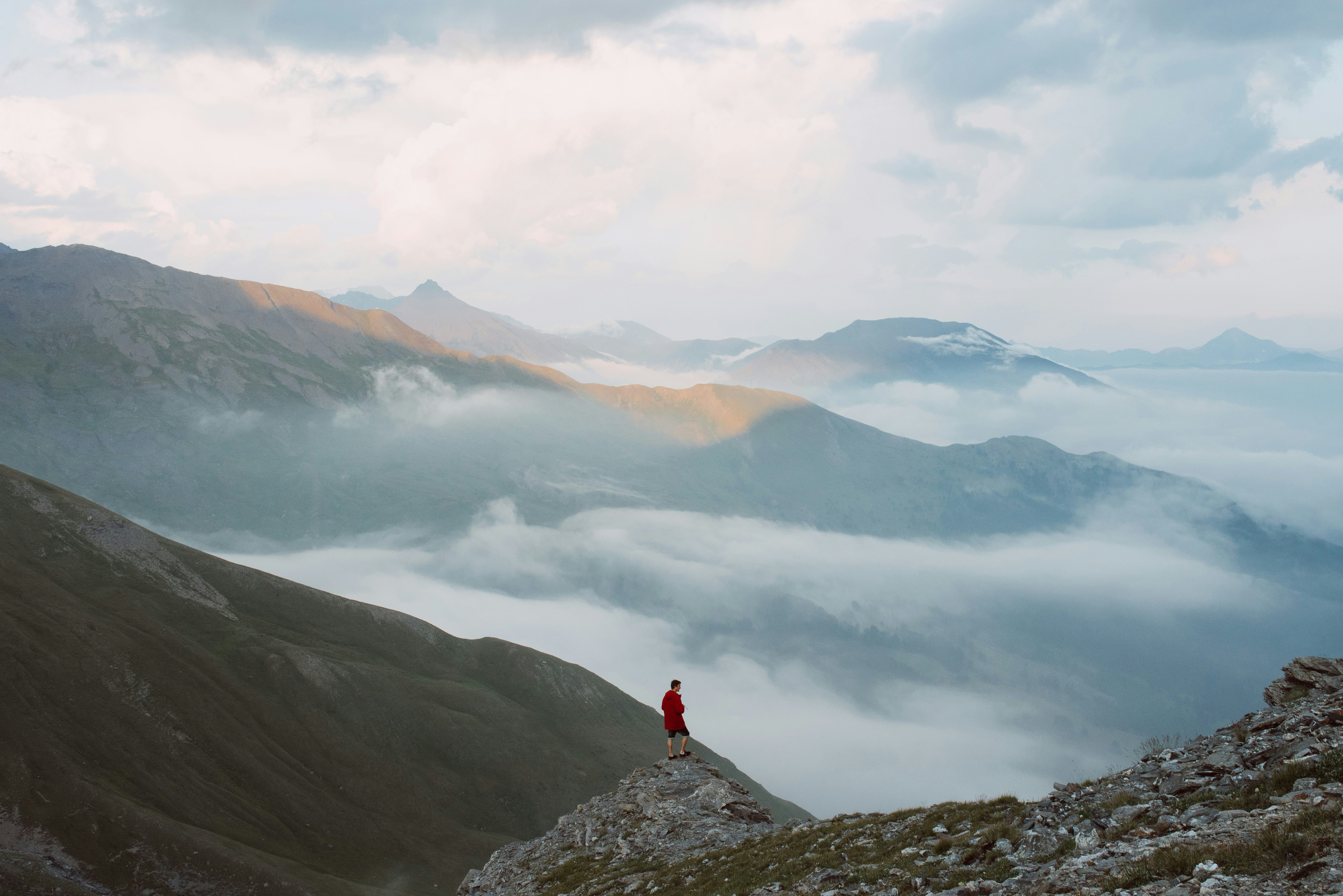 A lone figure in red on a ridge above a valley of cloud at dawn